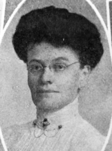 Black and white old-style image of a woman in a white turtle-neck blouse and rounds glasses.