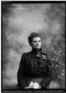 Photograph of a woman seated, looking right, with a ribbon tied in a bow around her neck.